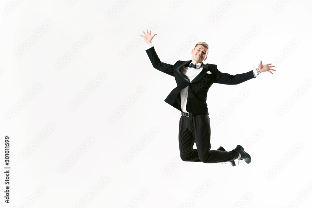 Portrait of young smiling handsome showman in tuxedo stylish black suit, studio shot jumping at white background. Businessman in jacket with bowtie Portrait of young smiling handsome showman in tuxedo stylish black suit, studio shot jumping at white background. Businessman in jacket with bowtie