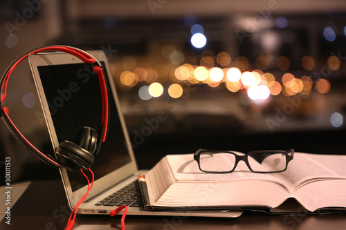 laptop with headphones and an open book with glasses, traditional reading and audiobook, beautiful bokeh
