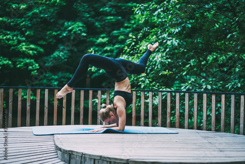 Attractive female training strength feeling motivated with goals while standing on hands in balance pose, young caucasian sportswoman practising yoga during outdoors workout keeping perfect body