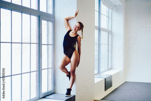 Full length portrait of energetic cheerful woman wear in trendy sport apparel looking at camera ready for new inscription at gym centre while standing near window and posing with smile indoors © BullRun
