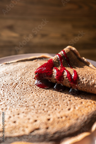 Chocolate pancakes with raspberry jam on a wooden background on a sunny morning. Vertical 
