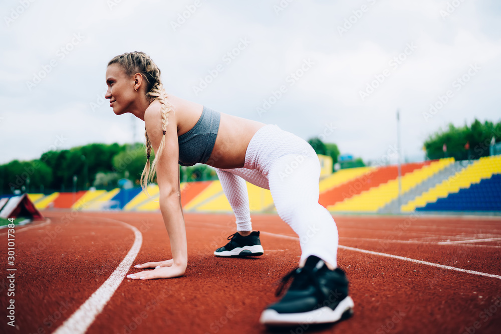 Female athlete stretching legs on racetrack