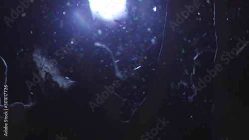 Slowmo shot of unrecognizable people dancing in dark nightclub or at concert as confetti falling on them from above photo