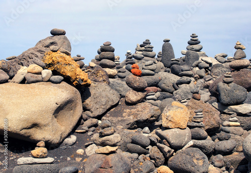 close up of towers of stacked pebbles and colored stones in a large arrangement on a black sand beach with blue sky