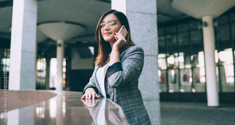 Portrait of charming female entrepreneur dressed in trendy jacket enjoying good roaming internet connection for making international conversation with colleague, concept of online communication