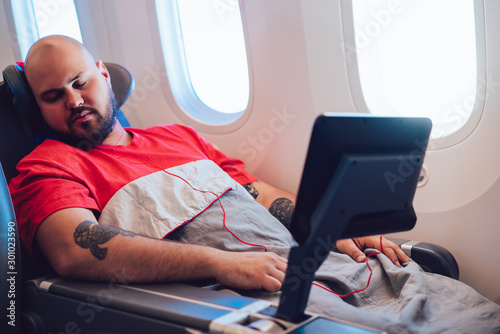 Caucasian adult man fell asleep during comfortable flight in economy business first class. Perfect beginning of vacation holidays. Male passenger resting in comfortable seat with large space for legs