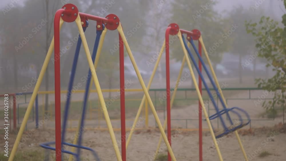 Swinging empty swing. Playground in the fog without people in a city park. Mysterious morning Swinging empty swing. Playground in the fog without people in a city park. Mysterious morning