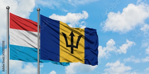 Luxembourg and Barbados flag waving in the wind against white cloudy blue sky together. Diplomacy concept, international relations.