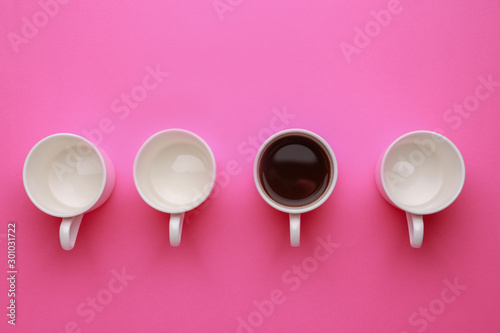 One cup of coffee among empty ones on color background. Concept of uniqueness