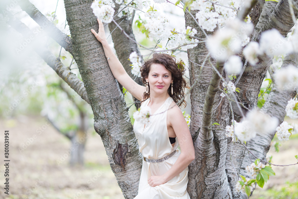 A portrait of beautiful young Caucasian woman with curly dark hair in blossoming orchard
