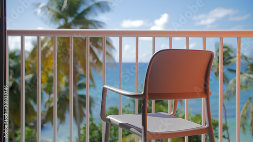 A chair on a balcony with a sunny beach in the background