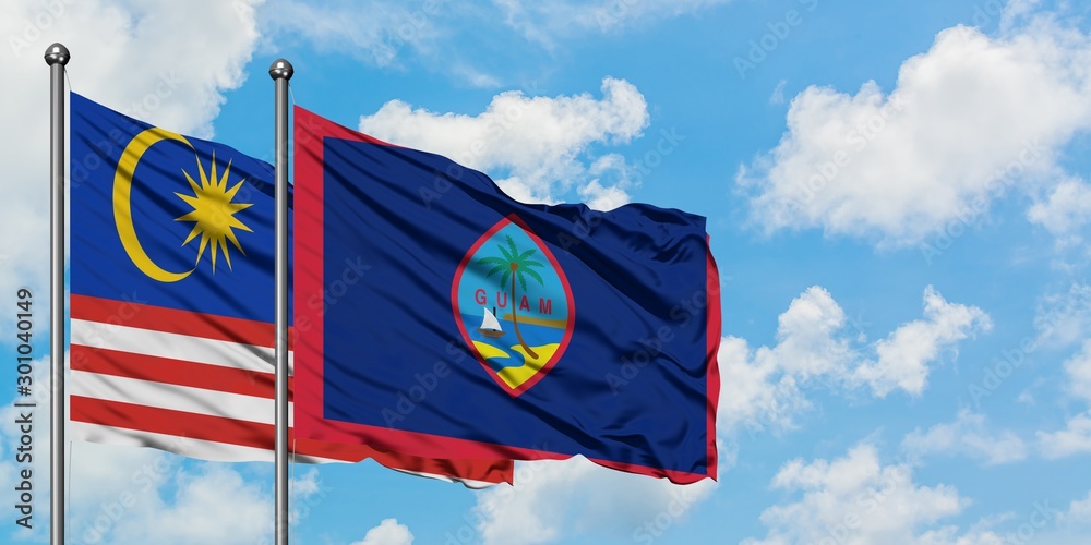 Malaysia and Guam flag waving in the wind against white cloudy blue sky together. Diplomacy concept, international relations.