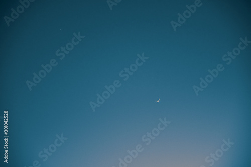 Small crescent moon and a tiny star in a vast evening sky.