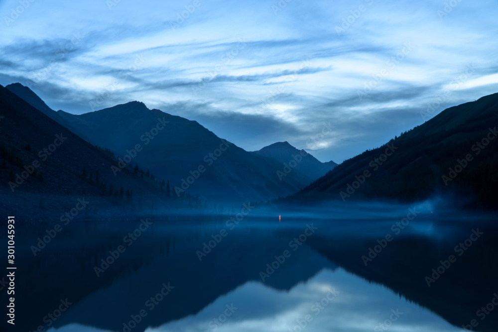 A mountain lake with a beautiful reflection at sunrise. Blurring due to fog is caused by water.