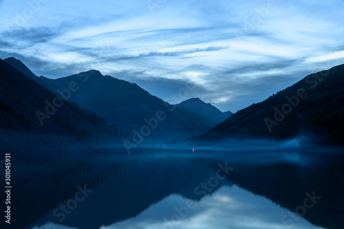 Fototapeta Naklejka Na Ścianę i Meble -  A mountain lake with a beautiful reflection at sunrise. Blurring due to fog is caused by water.