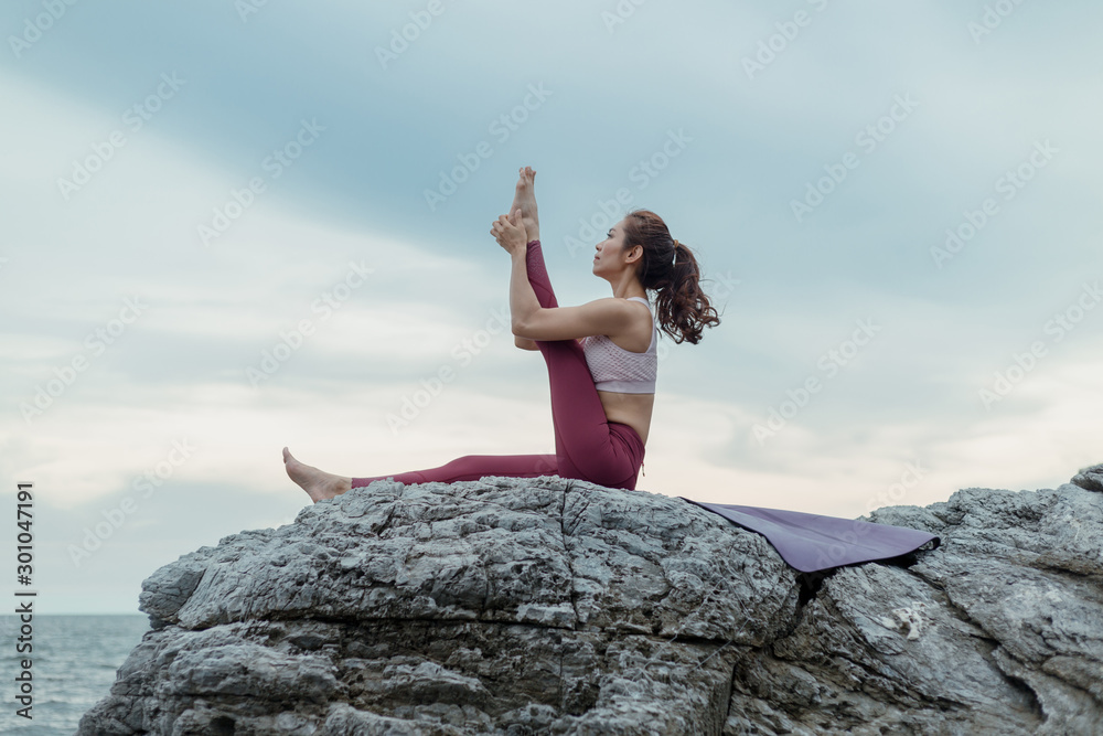 Young woman doing yoga exercise yoga master pose on the rock. Amazing yoga landscape in beautiful sky and enjoying sea view on wooden floor, concept for exercising, health care Young woman doing yoga exercise yoga master pose on the rock. Amazing yoga landscape in beautiful sky and enjoying sea view on wooden floor, concept for exercising, health care