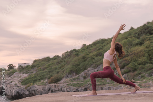 Side view Young women practicing yoga and practicing yoga postures Amazing yoga postures in the beautiful sky and enjoying the sea view on the wood floor Idea for exercise  health care