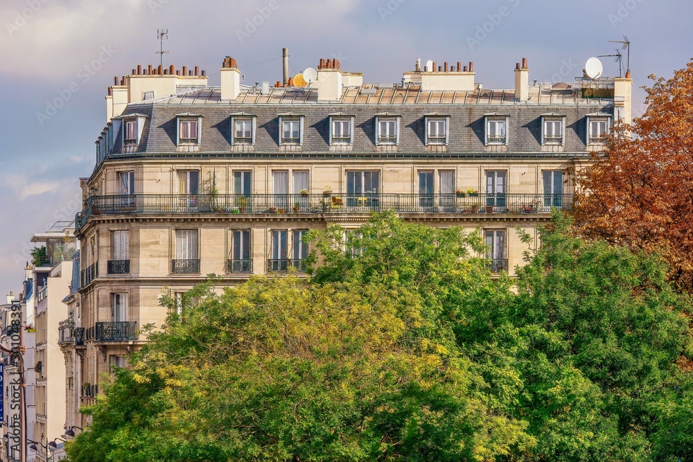 A traditional Parisian apartment building in a residential neighborhood, with large trees adding nature to the urban setting.