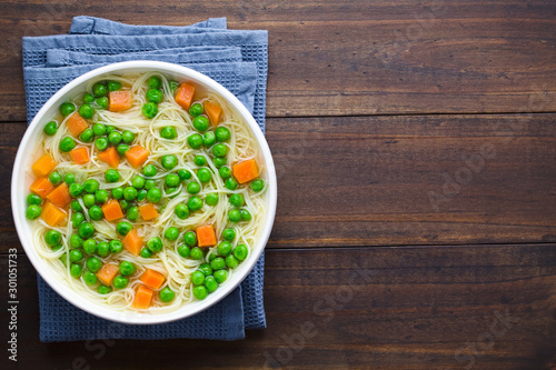 Fresh homemade vegetable noodle soup with carrot, peas, onion and angel hair pasta in white soup bowl, photographed overhead with copy space on the right side