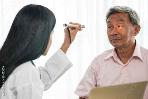 Doctor checking senior man patient eyes with flashlight in medical office