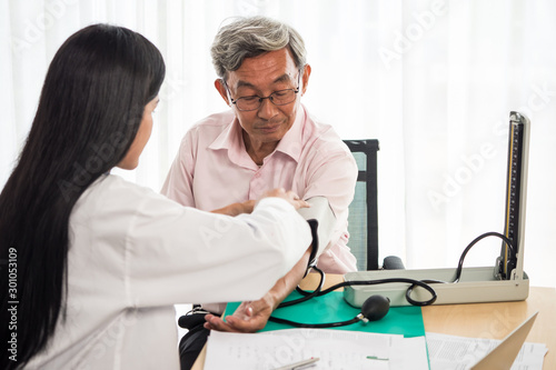 Doctor measuring blood pressure of elderly man in medical office.