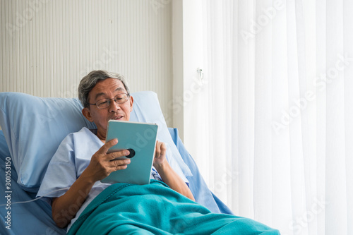 Tela Happy elderly patient sitting on bed and making video call with tablet at hospital