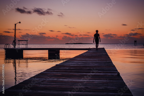Getting away from it all. Silhouette of a boy walking out on a dock in the Florida Keys. Watching the sunset over the horizon with the ocean in front of him.  photo