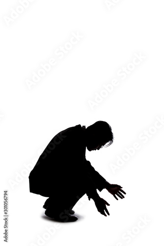 Silhouette of a backlit model posing as a businessman on a white background.  He is crouched on the ground like a detective looking or searching for something on the floor