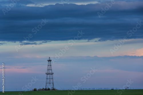 Old oil rig, profiled on sky with storm clouds, at sunset