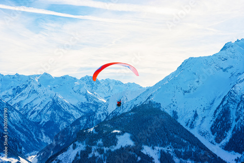 People paragliding on parachute in sky. Alps mountains on Penken Park ski resort in Tyrol at Mayrhofen of Zillertal valley in Austria in winter with snow. Austrian Alpine snowy slopes.