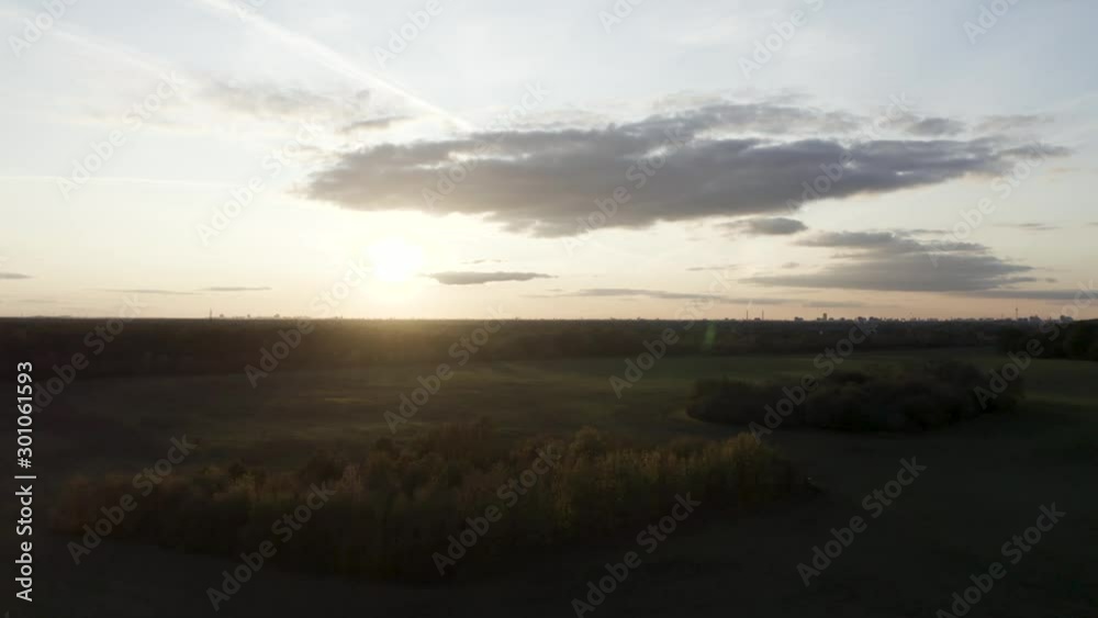 The drone flies smoothly upwards and shows an interesting, varied perspective on the city, the forest and the fantastic sunset in the background.