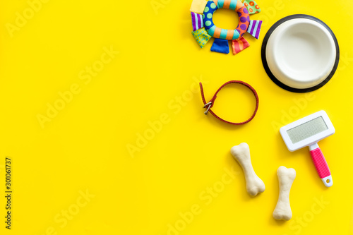 Set of treats and toys for pets with bones, collar and bowl on yellow background top view frame copy space