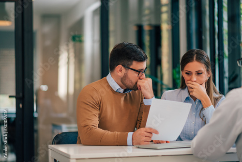Slika na platnu Portrait of a couple with financial problems looking at document in financial adviser's office