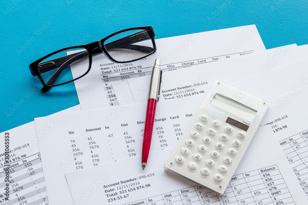 Taxes calculation concept. Financial documents, calculator, glasses on blue background Taxes calculation concept. Financial documents, calculator, glasses on blue background