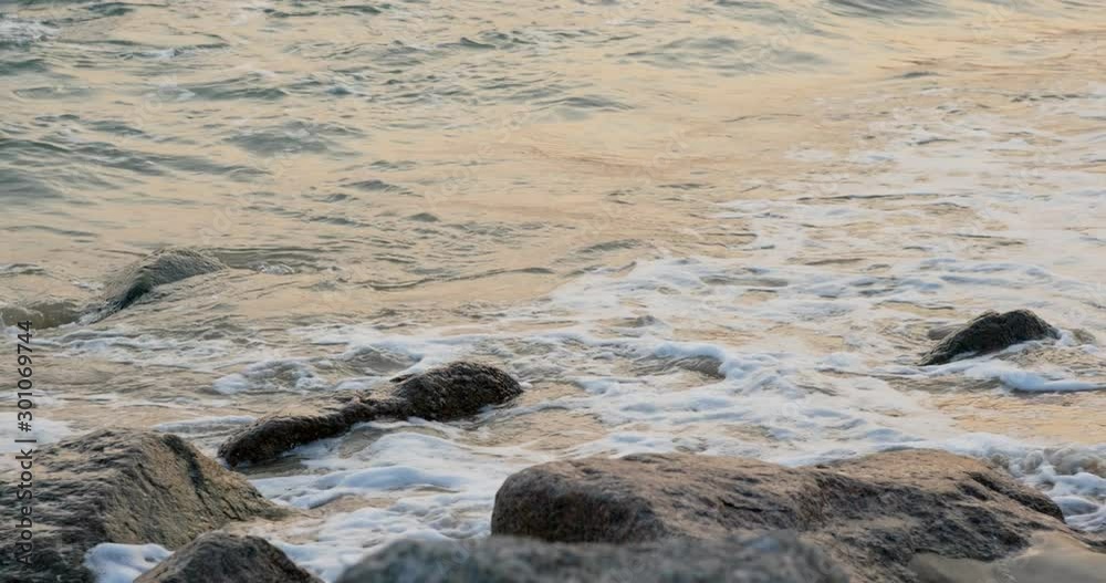 Sea wave on rock stone at sunset