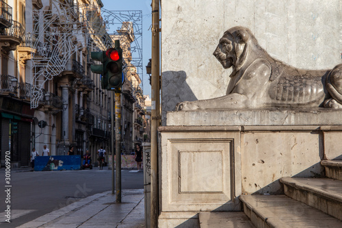 Palermo, Italy, September 19, 2019: Detail of a building with a lion on the stairs and the street in the background, a red traffic light and Christmas lights during the day