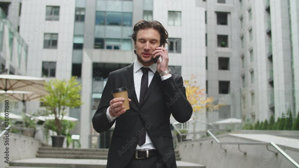 A young guy in a business suit is walking around the courtyard of an office building and is talking on the phone. A young guy in a business suit is walking around the courtyard of an office building and is talking on the phone.