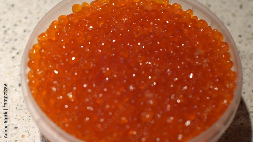 Packing red caviar shiny in the light. Plastic jar with red caviar of sea fish. Gifts of the sea. Transition from focus to sharp image. A slight movement of the frame. Close up Packing red caviar shiny in the light. Plastic jar with red caviar of sea fish. Gifts of the sea. Transition from focus to sharp image. A slight movement of the frame. Close up