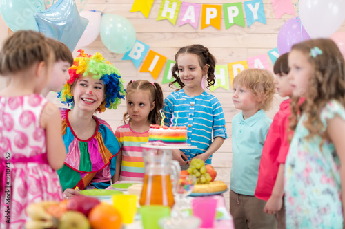 Birthday children party. Kids with clown gathered around birthday cake