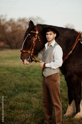 handsome groom in a hat stroking a horse. man with a horse
