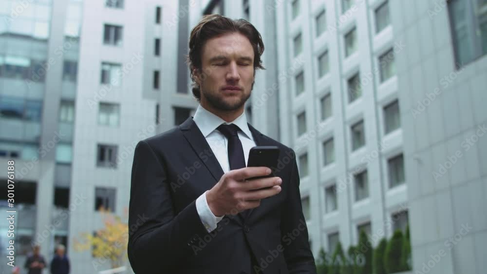 An office employee writes SMS in the courtyard of a modern business center. The man is thoughtful and periodically looks around. An office employee writes SMS in the courtyard of a modern business center. The man is thoughtful and periodically looks around.