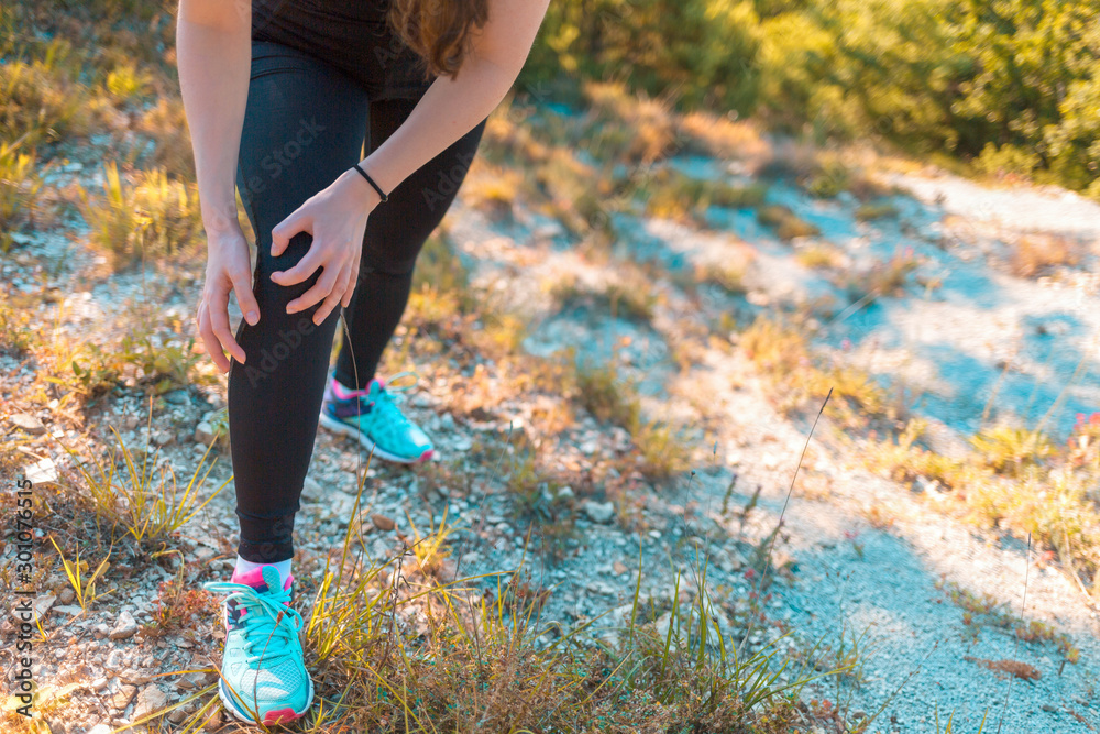 A young athletic woman is experiencing pain in her leg due to an injury while Jogging on rough terrain. Concept of sports and sports injuries A young athletic woman is experiencing pain in her leg due to an injury while Jogging on rough terrain. Concept of sports and sports injuries
