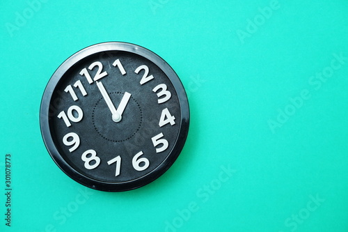 Black round clock showing Ten o'clock on green background