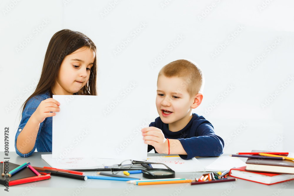 two cute smiling schoolchildren with blank sheet of paper in hands two cute smiling schoolchildren with blank sheet of paper in hands
