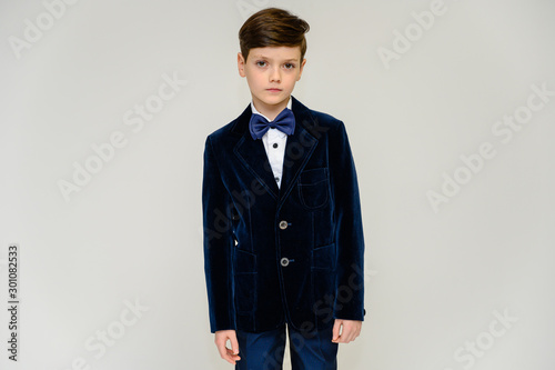 Concept boy teenager shows imitates entertainer behavior on stage. Portrait of a child on a white background in a dark blue concert suit. Standing in front of the camera in poses with emotions.