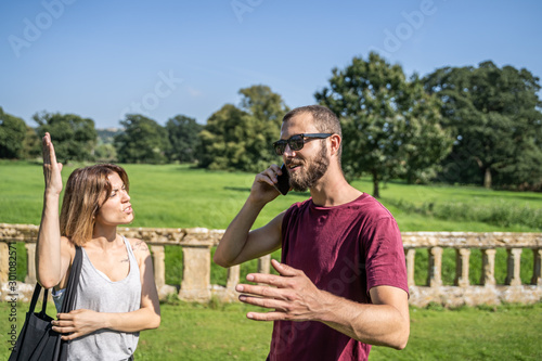 Girl arguing with raised hand with a boy who talks to the mobile in a garden
