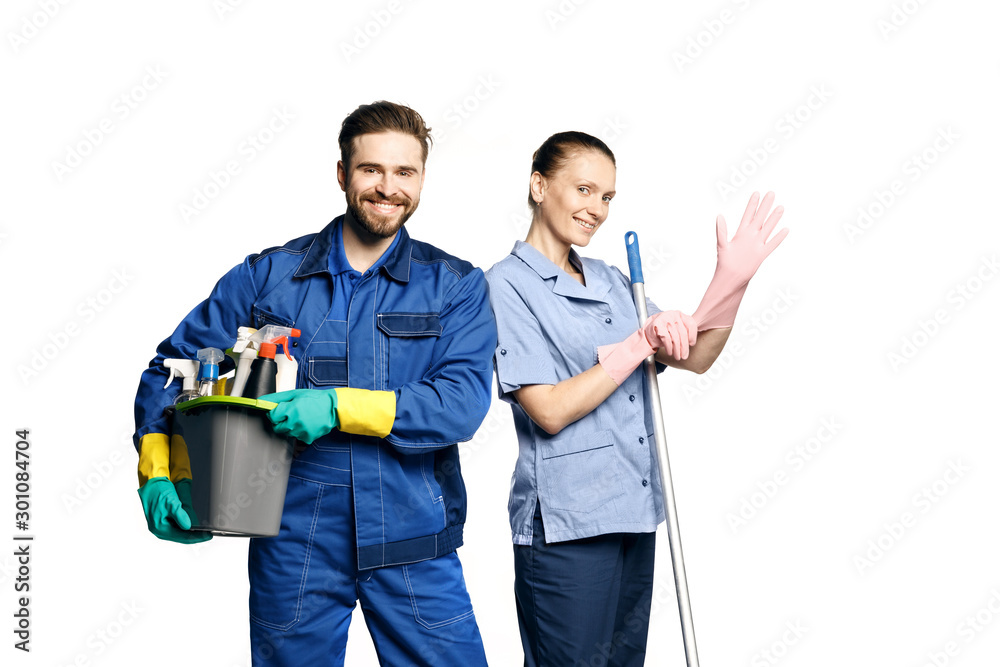 Attractive young woman and man  in cleaning uniform and rubber gloves holding  a mop and  a bucket of cleaning products in his hands, isolated on white background. - obrazy, fototapety, plakaty 