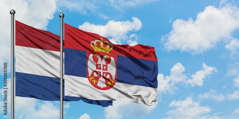 Naklejka premium Netherlands and Serbia flag waving in the wind against white cloudy blue sky together. Diplomacy concept, international relations.