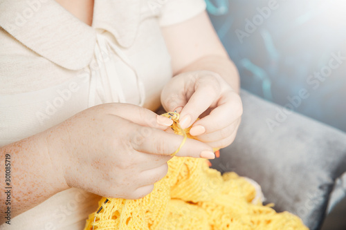 Female hands in freckles knit a yellow openwork blouse with knitting needles.
