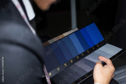 The dressmaker is choosing the fabric to cut the suit. Customers are choosing the color of the fabric in order to tailor the suit.